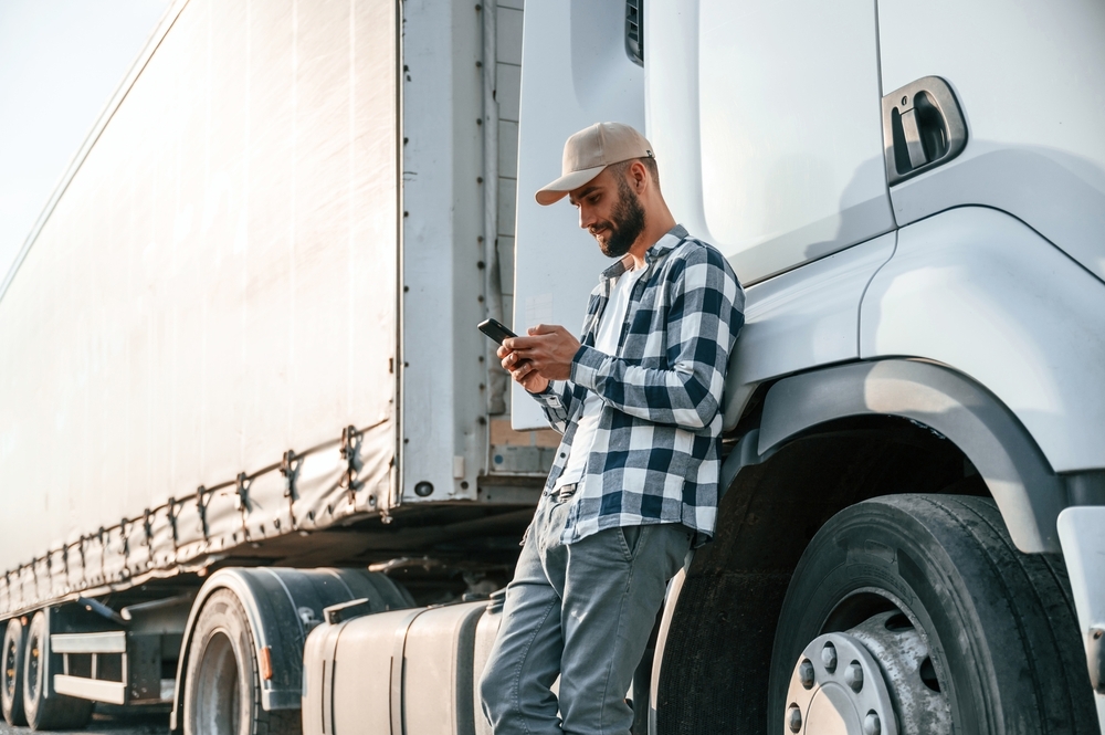 Truck driver leaning against his rig, checking his phone